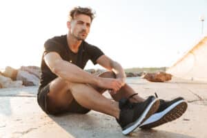 Man sitting on the ground with legs stretched out, considering knee replacement surgery.